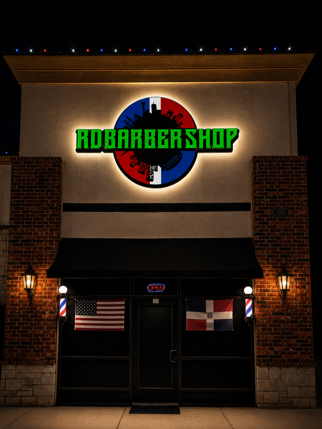 Fachada iluminada de RD Dominican Barbershop de noche.